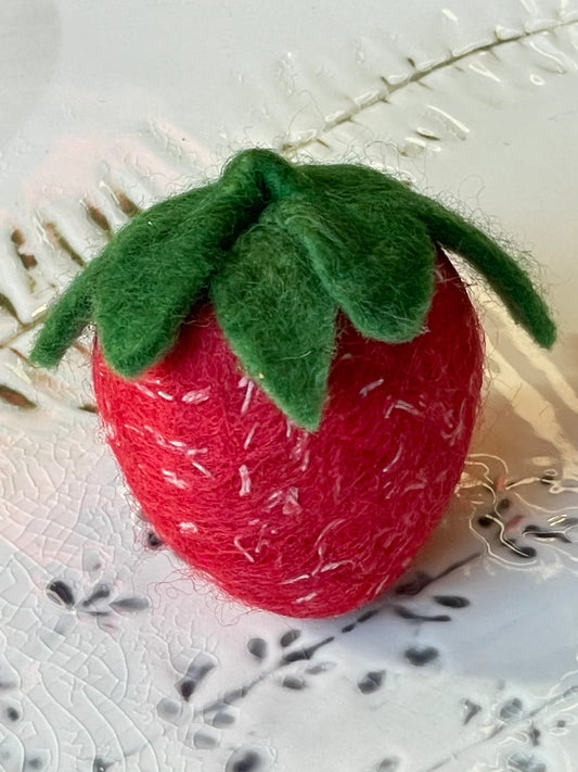 Red felt strawberry soap with green leaves on a textured white background