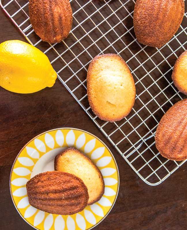 Madeleines on a cooling rack with a lemon and a decorative plate on a wooden surface
