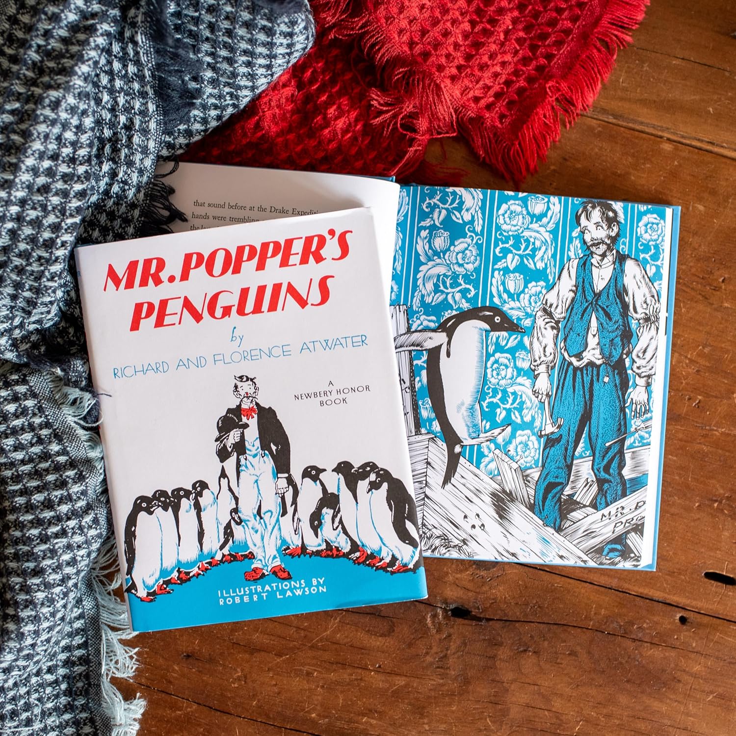Book titled 'Mr. Popper's Penguins' on a wooden surface with a red and gray textured fabric.