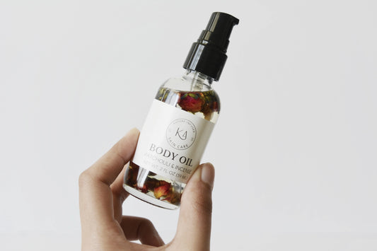 Hand holding a bottle of body oil with a Karomni label against a light background