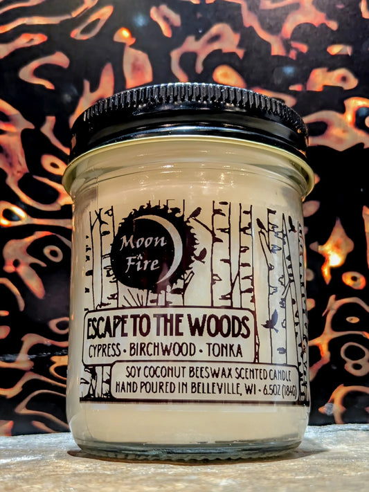 Candle jar labeled 'Escape to the Woods' with decorative nature background and Moonfire branding.