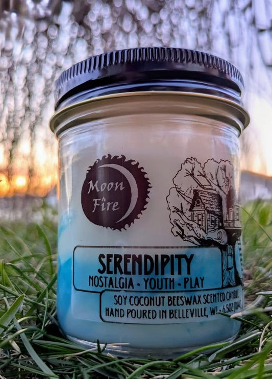 Candle jar labeled 'Moon Fire' with 'Serendipity' description on grass